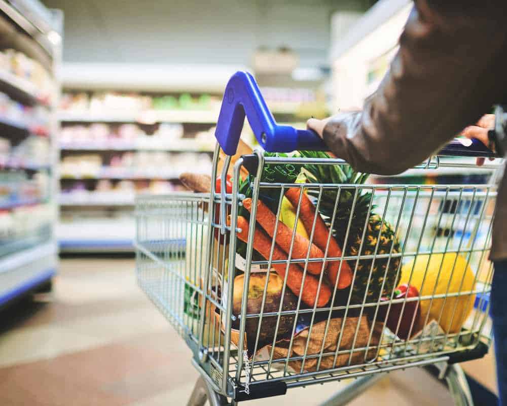 Woman pushing shopping cart down grocery store aisle
