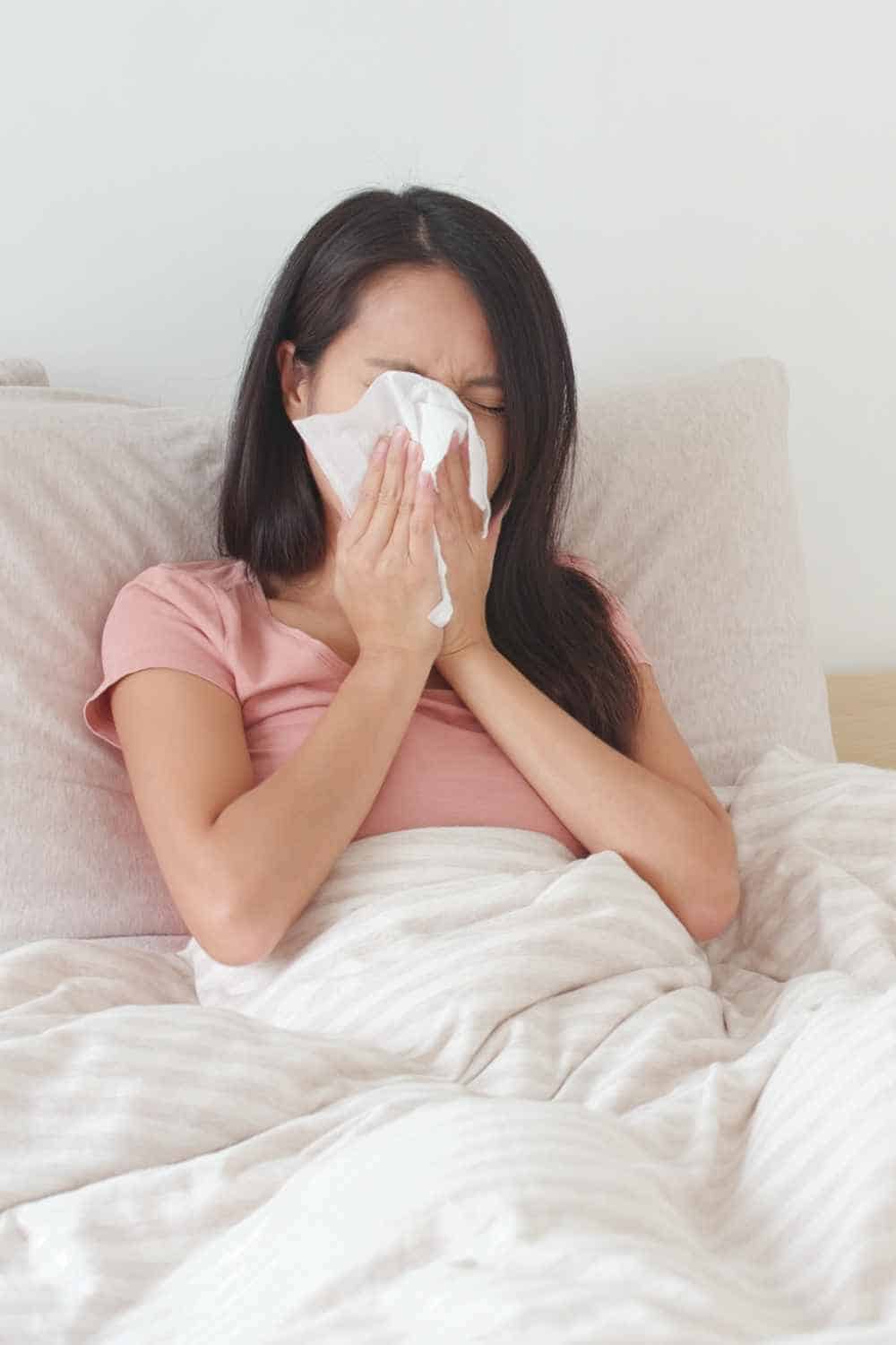 Woman sitting in white bed blowing nose