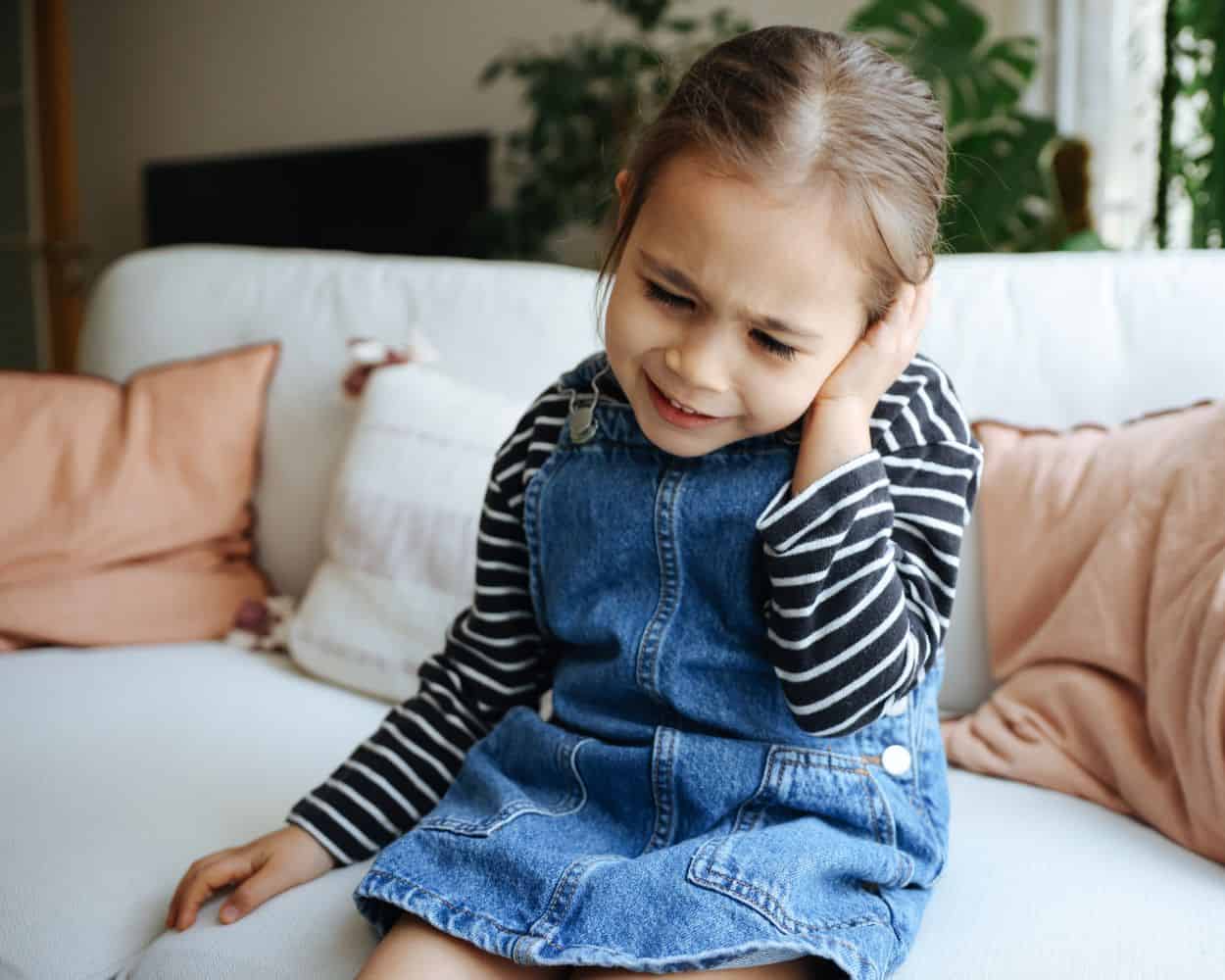 Little girl sitting on couch holding ear in pain