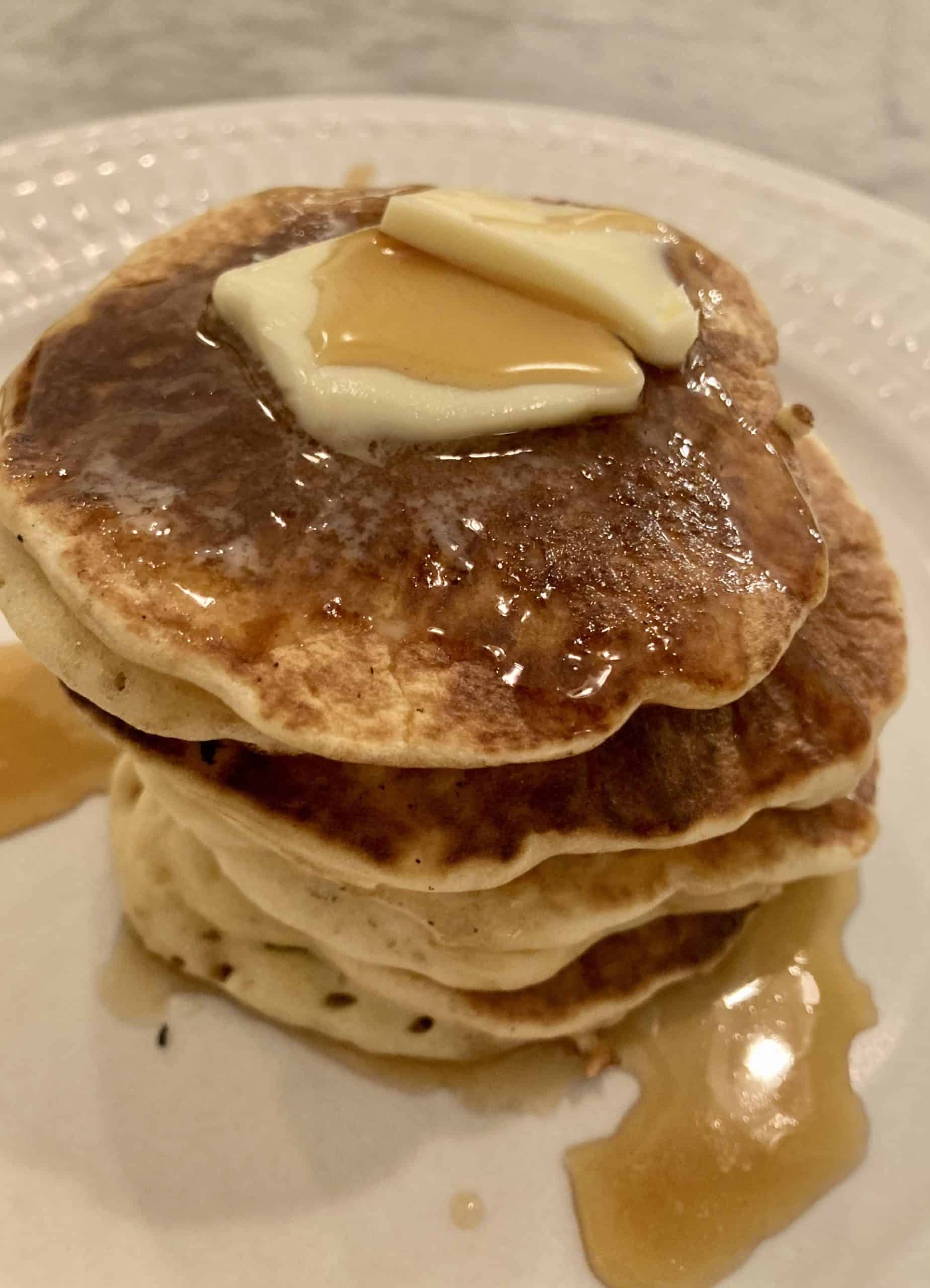 Pile of pancakes on white plate with butter and syrup